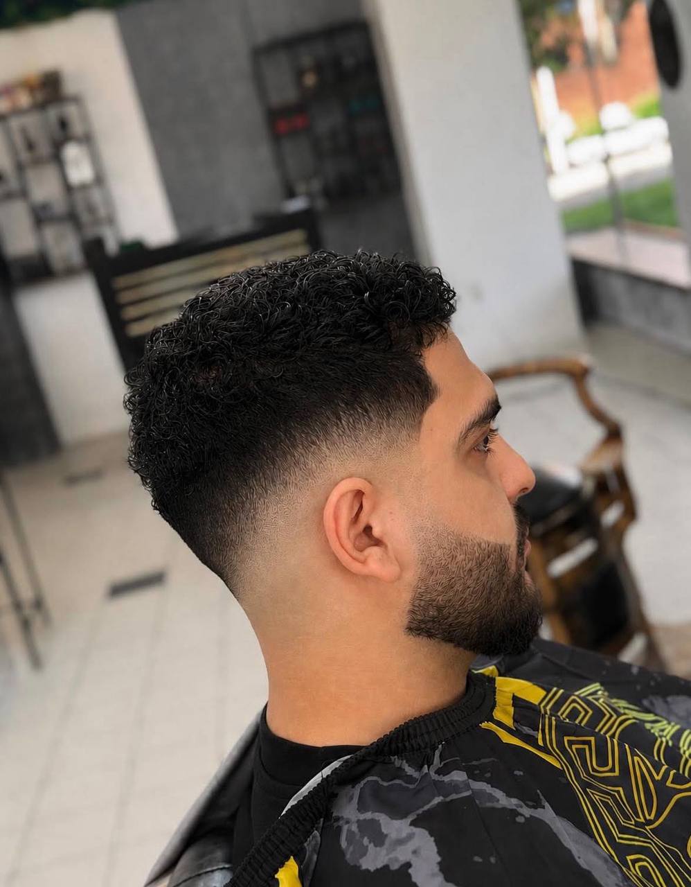 Krullend haar met mid fade en verzorgde baard bij Nobar Barber